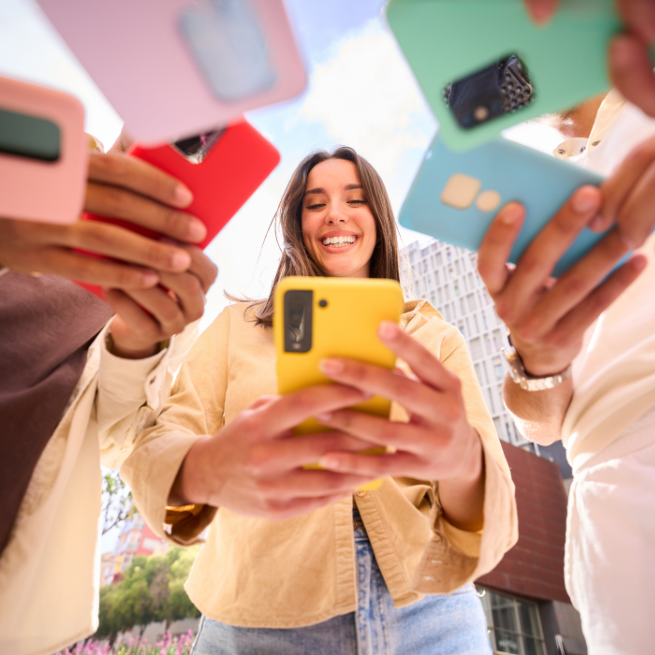 Eine Gruppe junger Menschen steht im Kreis zusammen. Alle schauen auf ihre Smartphone. 