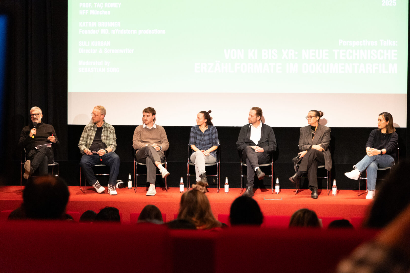 Ein Panel auf dem DOK.fest. Sieben Personen sprechen auf einer Bühne. 